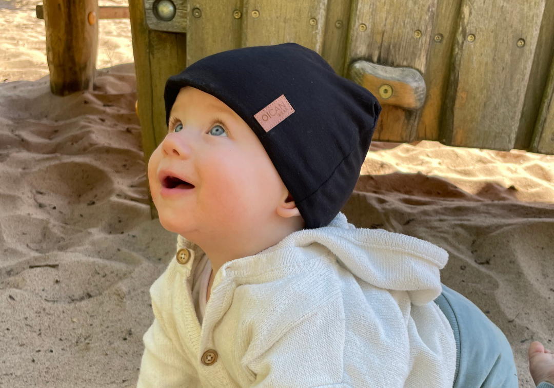 Barn kryper i sanden med en svart SafeHat på huvudet.