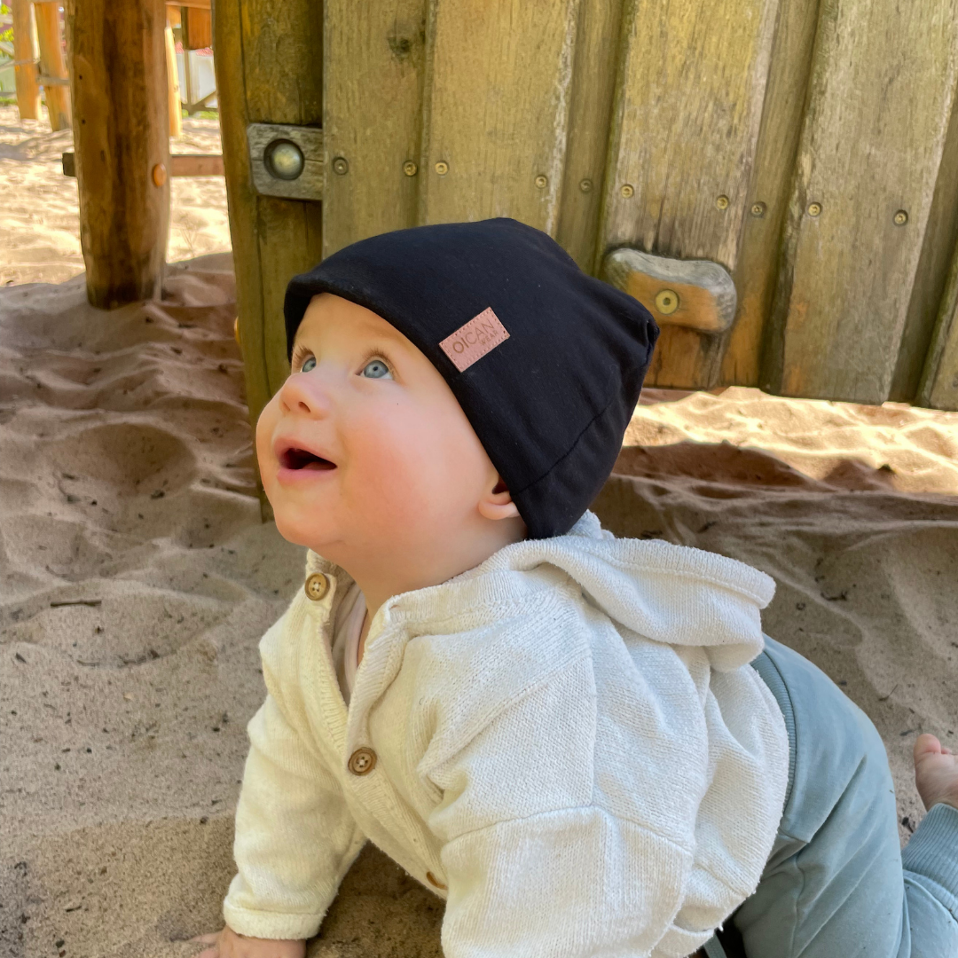 Barn kryper i sanden med en svart SafeHat på huvudet.