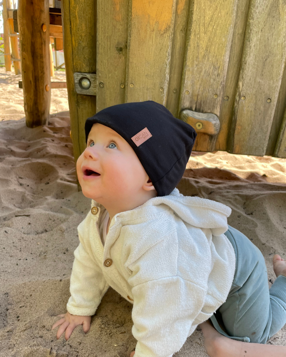 Barn kryper i sanden med en svart SafeHat på huvudet.